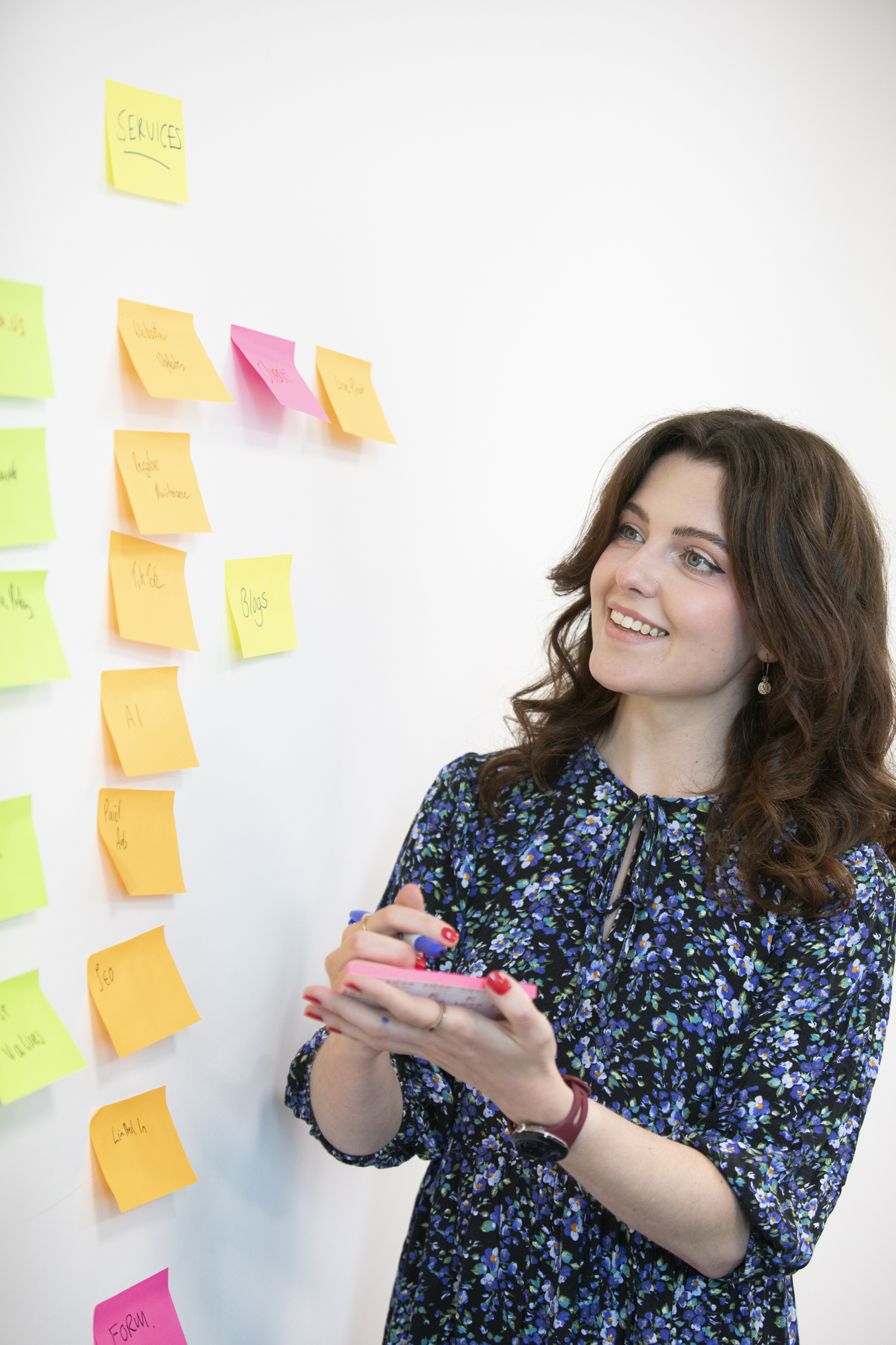 A Cyberlogical team member smiling as she plans services on a wall of sticky notes