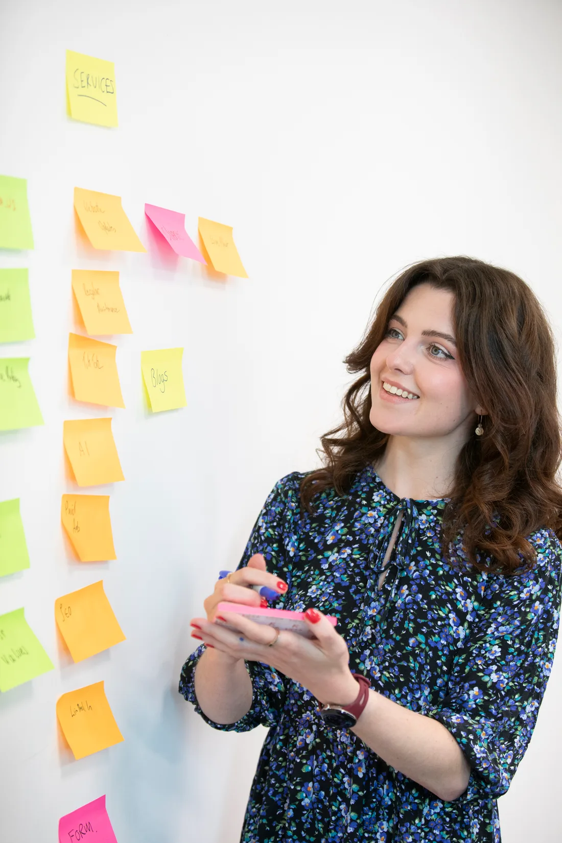 A Cyberlogical team member smiling as she plans services on a wall of sticky notes